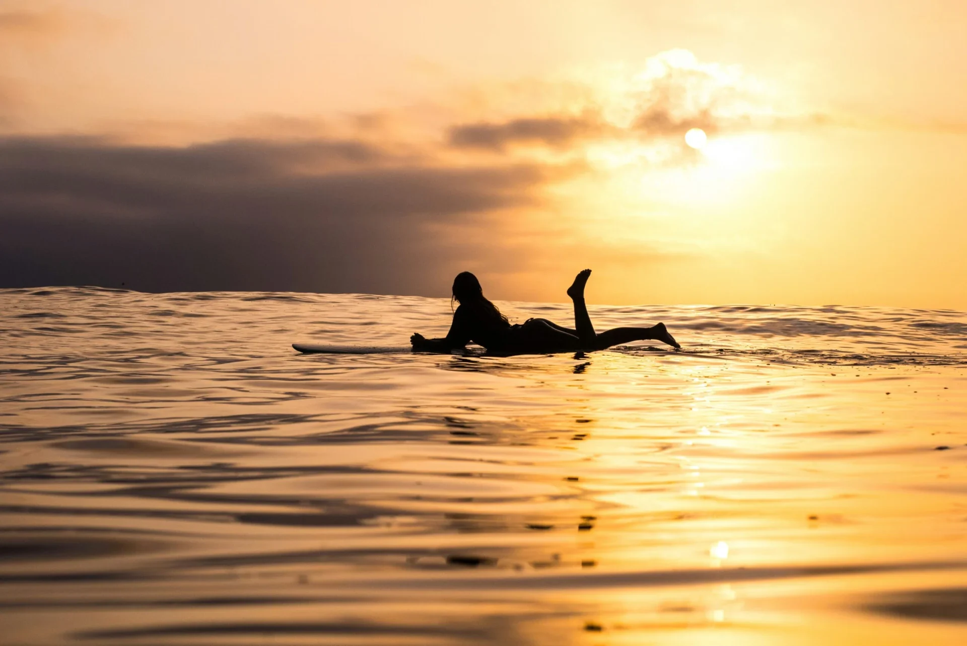 Surfer paddling at sunset on ocean waves.